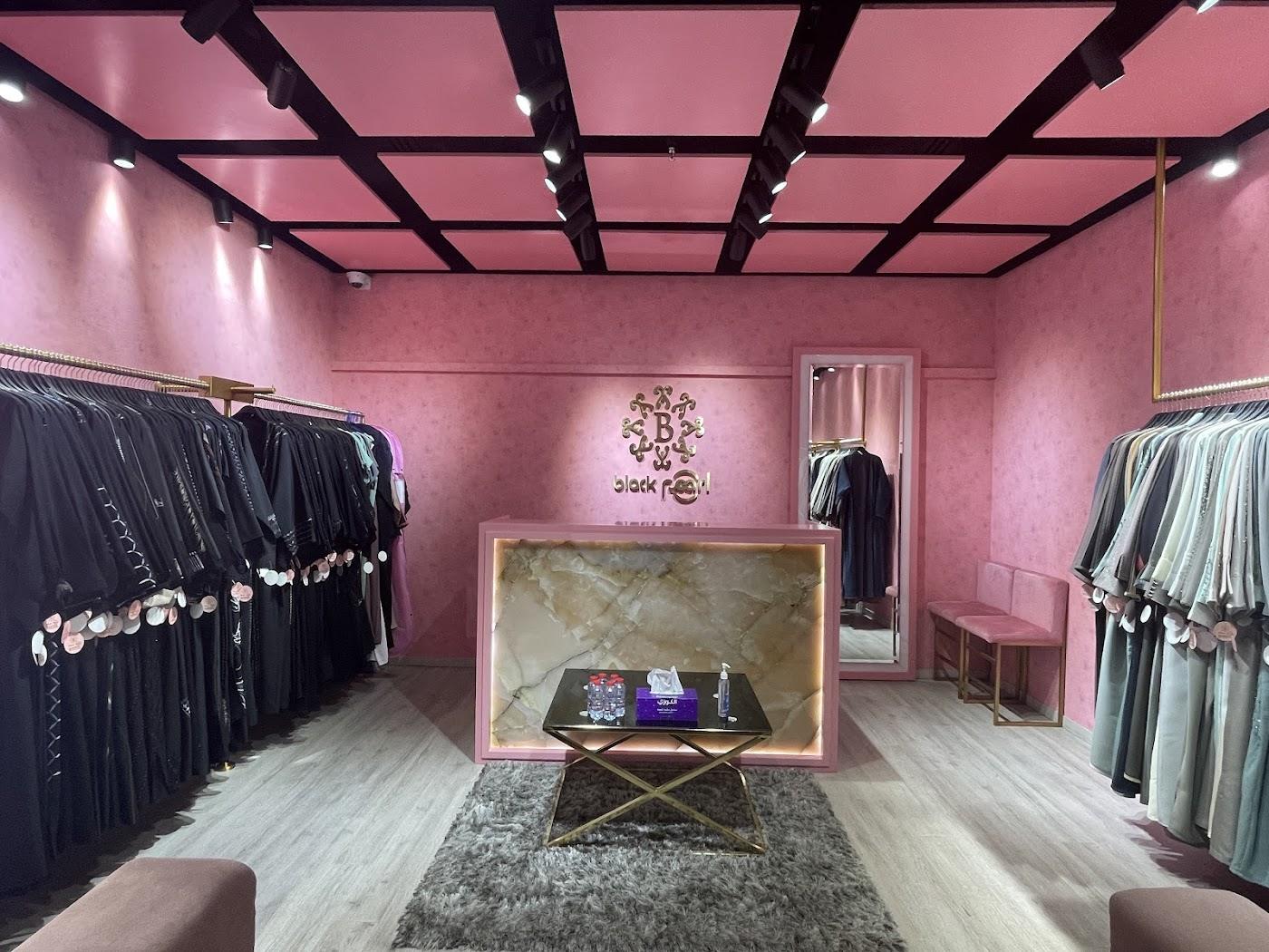 Inside Black Pearl at J3 Mall: pink walls, black ceiling beams, abayas on rails each side and an onyx counter under the gold logo